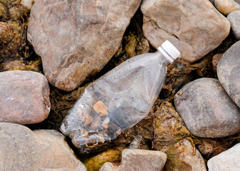 A transparent bottle is lying on the river stones. Garbage near the river