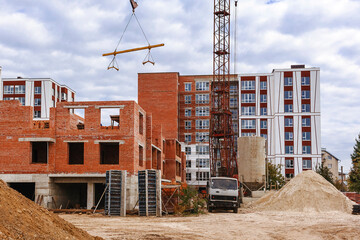 Сrane lifts the beam, Pile of sand and shovel at the construction site. cobstruction site background with built and unfinished houses