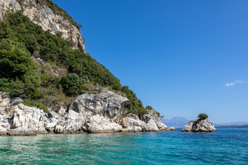 Fototapeta na wymiar Turquoise Ionian Sea with scenic green cliffs, rocks in water and bright sky. Nature of Ormos Desimi, Lefkada island in Greece. Summer vacation idyllic travel destination