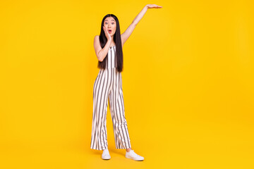 Full length body size photo girl amazed touching cheek in striped overall showing size with hand isolated vibrant yellow color background
