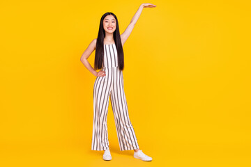 Fototapeta na wymiar Full length body size photo girl smiling in striped overall showing height with hand isolated vibrant yellow color background