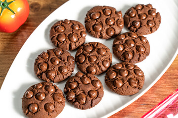 Close up dark brown chocolate chips cookies on plate. Fresh home made chocolate cookies. Eggless Baked chocolate cookies for vegetarian people.  