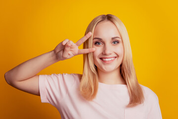 Portrait of dreamy charming pretty cute girl show v-sign cover eye on yellow background