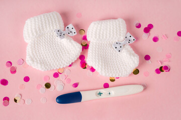 A positive pregnancy test and baby booties on a pink background. Waiting for the baby.