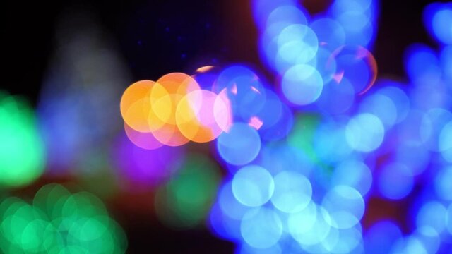 Defocused bokeh lights. Blurry Christmas lights festive background. A blurry image of a Christmas tree decorated with colorful lights in the city square. Bokeh.