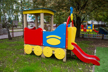 A wooden train of bright red, blue and yellow colors against a background of green trees and...