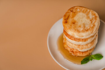 Cottage cheese pancakes on a plate with honey and mint on a beige background. Healthy and delicious morning breakfast. Traditional Russian food. Copyspace.