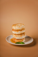 Cottage cheese pancakes on a plate with honey and mint on a beige background. Healthy and delicious morning breakfast. Traditional Russian food. Copyspace.