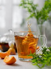 Tea with herbs and tangerine. A splash of tea. A slice of tangerine falls into the tea. Light background