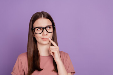 Young woman in glasses thinking look empty space isolated on purple background