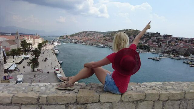 Woman on the walls of Kamerlengo castle of Croatia. Aerial view with St. Lawrence cathedral and bell tower. Trogir historic fortified city on a small island on the coast of Adriatic sea.