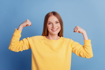 Fototapeta premium Portrait of fit slim sportive active lady show hand muscles toothy smile on blue background