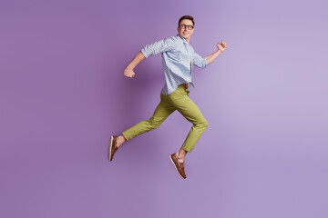 Fototapeta na wymiar Portrait of jumper energetic active guy jump run look back empty space on violet background