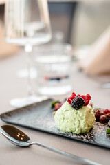 Ice cream on a black plate with fruits and sauce at a restaurant