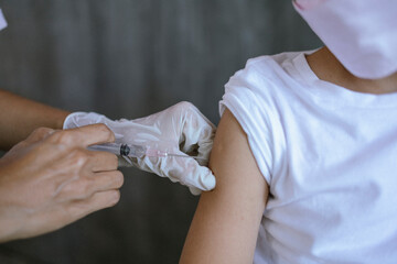Close up Doctor injecting vaccination into shoulder against COVID-19 for Asian children