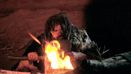Prehistoric caveman looks at fire and holding spear in cave