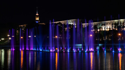 Fototapeta na wymiar Multicolored musical fountain on a river at night. The fountain in the night from illumination. Long exposure.