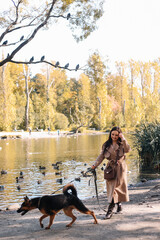 A happy funny girl in a casual coat walks with her dog, pet and best friend in the autumn forest by the water in nature in fall outdoor, selective focus