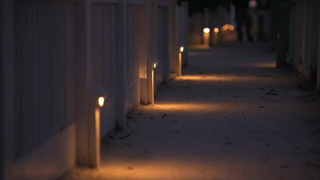 Beach wooden architecture with person man person feet standing on path way at dark night evening lamps lights row by vacation rental property houses buildings