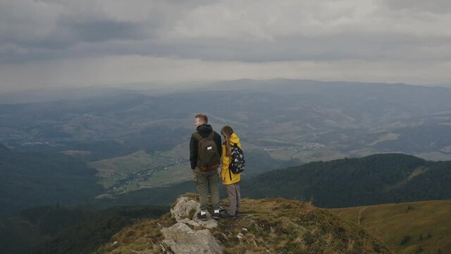 Aerial video shooting from a quadrocopter of the Mountain landscape. Young couple, a man and a woman, stand on the top of the mountain and look at the valley. Beautiful view