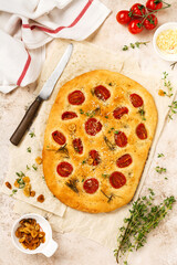 Italian traditional focaccia bread baking with with cherry tomatoes, parmesan and rosemary on light brown background. Top view