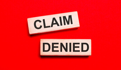 On a bright red background, there are two light wooden blocks with the text CLAIM DENIED