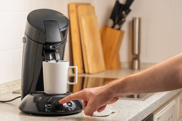 Male hand pressing the power button on the coffee maker in the kitchen