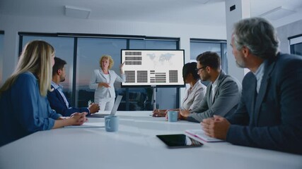 Blonde mature female manager giving presentation at meeting to her team. Modern open space office interior.