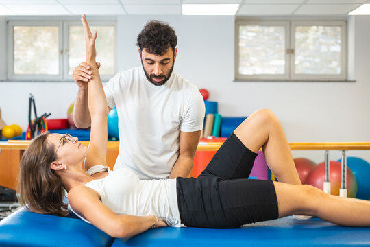 Woman laying on the back and doing upper body exercises with the assistance of a male physiotherapist.