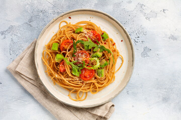 Spaghetti pasta with pesto, avocado and tomatoes in rustic white plate. Raw vegan food concept. Top view.