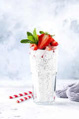 Fresh healthy milkshake yogurt with chia seeds and strawberries in a glass beaker against a gray concrete background. Selective focus