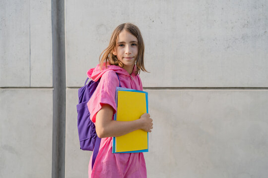 Teenage girl with a schoolbag and notebooks in front of gray wall
