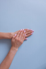 Elegant hands with pink manicure on a blue background, clean color, white skin.