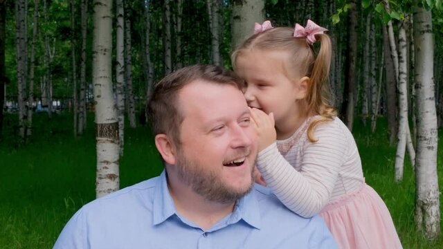 little daughter, 3 years old, tells her daddy in her ear and laughs. The concept of a happy childhood, fatherhood, parenting. A trusting relationship between parents and children. Fathers day