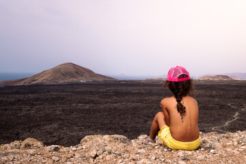 Unrecognizable girl contemplating volcanoes under light sky
