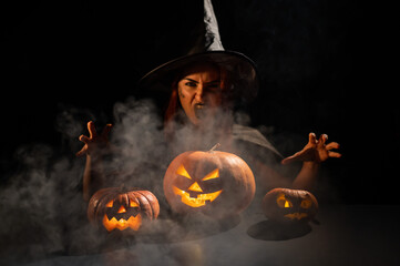 The evil witch casts a spell on pumpkins. Portrait of a woman in a carnival halloween costume in...