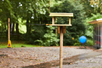 Wood birdhouse feeder stood on a wooden stand in a park next to a safety cone and life vest storage
