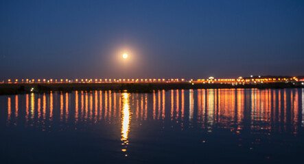 Obraz premium pier at sunset, Illumination at the dam of the hydroelectric power station as a background and moon road. Selective focus.