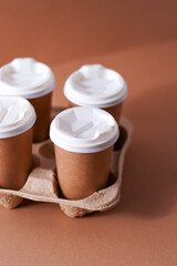 Paper cups in a cup holder for takeaway coffee. Paper cup with a drink. Disposable tableware. Eco cardboard recyclable. Brown background. Copy space