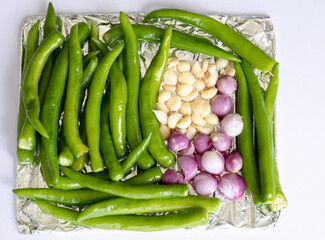 Top view of raw green chilli, garlic and onion on aluminum foil tray before place into oven to...