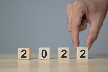 Hand of man putting wood cube 2022. New year concept.