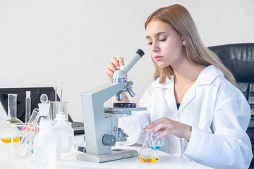 The biologist looks through microscope. Woman biologist. Laboratory worker with microscope. blonde...