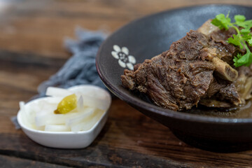 The food made of beef is in the bowl on the cloth of the wooden table
