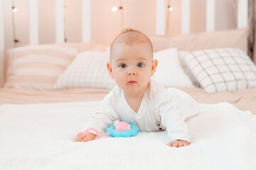 a baby in a white jumpsuit is lying on a bed with a rattle at home