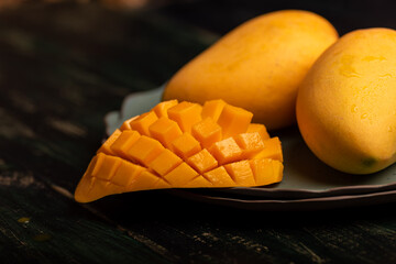 Cut and complete mangoes on a plate in a dark environment