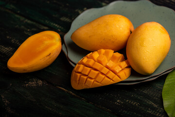Cut and complete mangoes on a plate in a dark environment