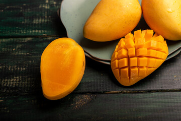 Cut and complete mangoes on a plate in a dark environment