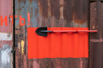 A red shovel hangs on the industrial metall wall on a stand for fire fighting equipment