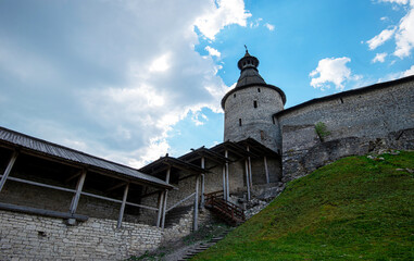 The fortress wall of a medieval fortification with towers against a bright blue sky.