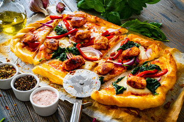 Pizza with white chicken nuggets, pepper, red onion, spinach and mozzarella on wooden background
